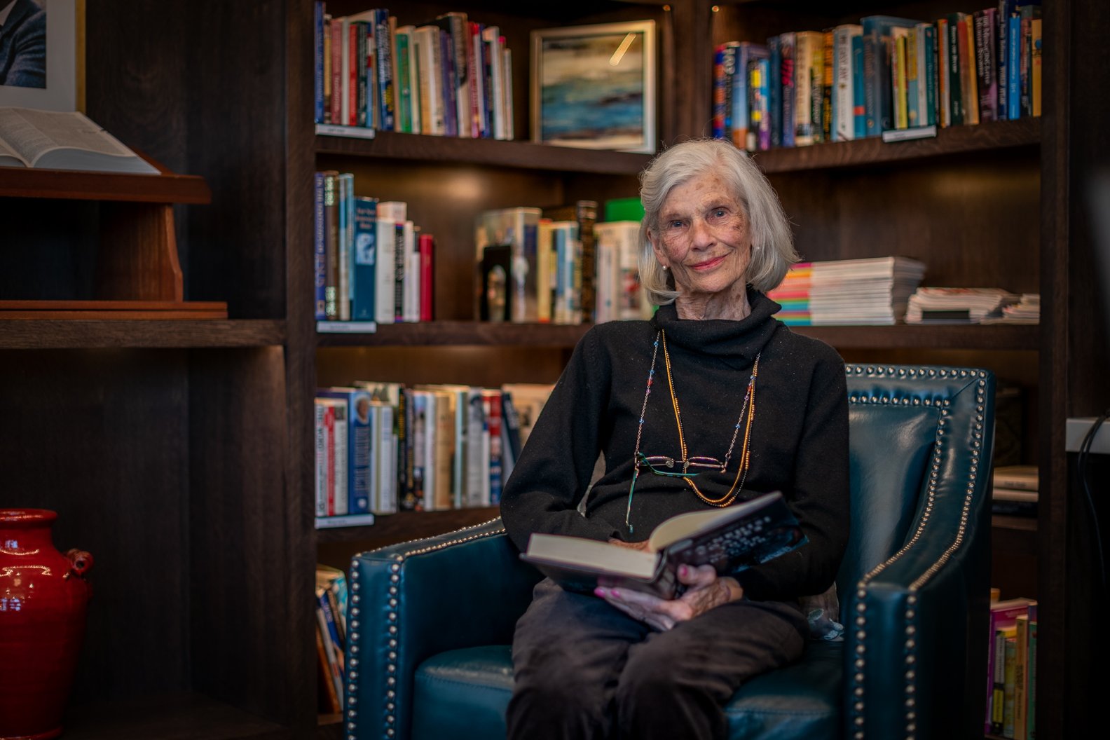 Woman reading book in library chair books shelves community room assisted living senior apartments residence golden valley mn